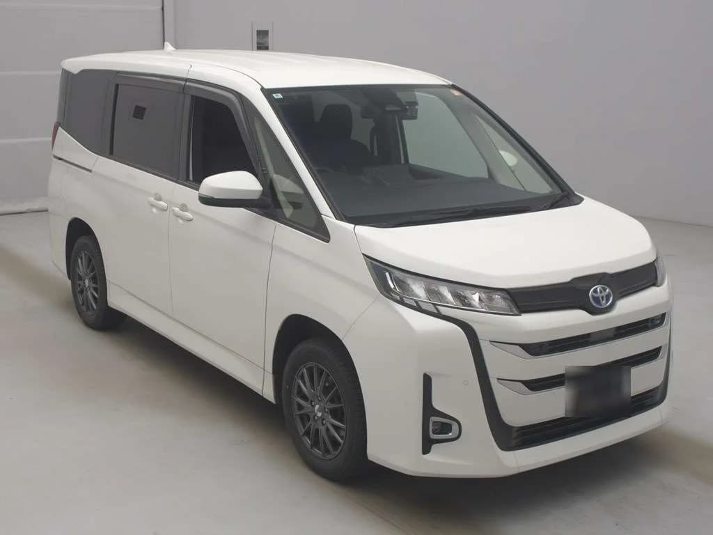 Toyota Noah minivan - Front-right exterior view in a studio setting with white paint, black grille, and dark multi-spoke alloy wheels