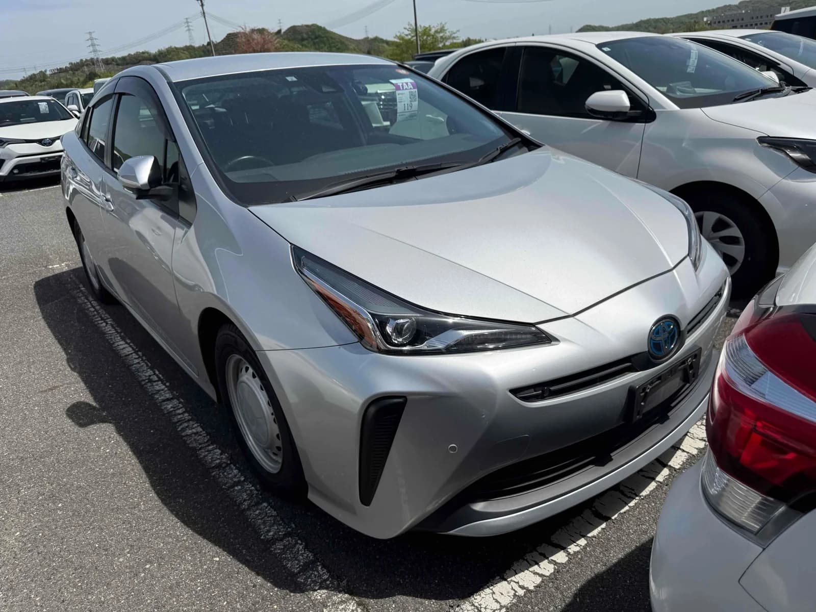 2021 Toyota Prius hybrid in silver metallic - front-right 3/4 view with slim LED headlights, blue hybrid Toyota badge, vertical air intakes, and window visors
